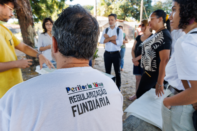Até o momento as ações de regularização fundiária contemplaram quatro comunidades, somando 246 unidades habitacionais (Foto: Ribamar Neto / UFC) Imagem: pessoa usando camisa com os dizeres Regularização Fundiária