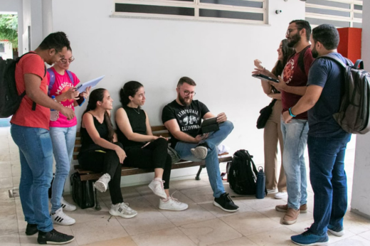 Para candidatos à renovação do auxílio, há requisitos como ter aprovação superior a 50% nas disciplinas do semestre anterior; não ter reprovação por falta nem nas disciplinas de estágio e TCC (Foto: Ribamar Neto/UFC) Estudantes interagindo. Três estão sentado no banco, três estão em pé á direita e dois em pé à esquerda