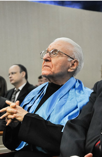 Prof. Emílio Recamonde Capelo recebeu o título de Professor Emérito da UFC em cerimônia realizada em 9 de dezembro de 2014 (Foto: Guilherme Braga/ UFC Informa) Imagem: Homem idoso, com cabelos brancos, sentado em auditório e vestido com roupa preta e capa azul