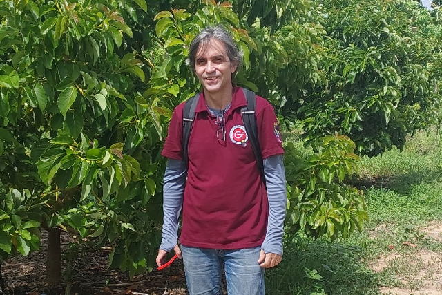 Professor concursado da UFC desde 2005, Márcio Cleber teve atuação destacada na área de fruticultura tropical, deixando contribuições na pesquisa e na formação de centenas de profissionais egressos do CCA (Foto: arquivo pessoal) Imagem: homem com cabelos lisos e parcialmente grisalhos posa para foto em um ambiente ao ar livre, cercado de verde e plantas. Ele veste camisa polo vermelha por cima de uma camisa de malha de manga longa, e calças jeans