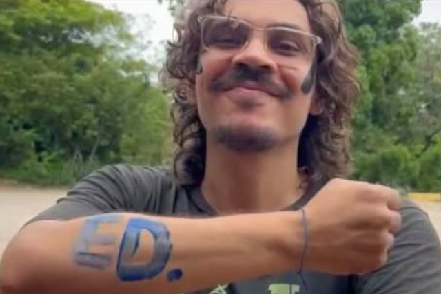 Integrante do movimento estudantil, Luan Gomes marcou muitos colegas pela sua dedicação às lutas na universidade (Foto: acervo pessoal) Imagem: Homem sorrindo mostra o antebraço com a palavra “ED.” pintada em azul. Fundo com árvores ao ar livre.
