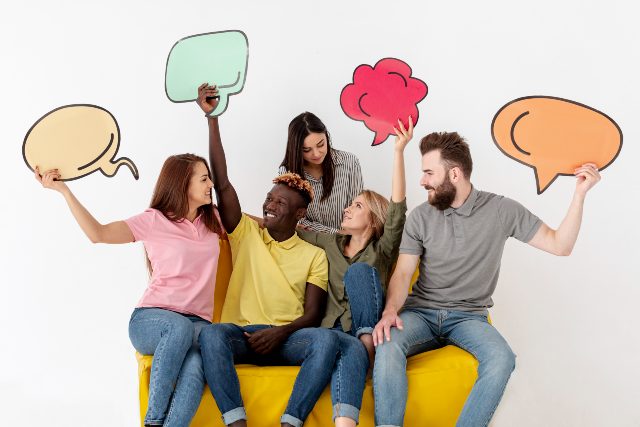Evento foi criado pelo Grupo de Estudos e Pesquisas em Linguística Aplicada (Gepla) da UFC (Imagem: Freepik) Trata-se de uma foto de cinco pessoas sentadas em um sofá amarelo, sorrindo e segurando balões coloridos em formato de diálogo. Ao fundo, uma parede branca, sugerindo comunicação, troca de ideias e trabalho em equipe.